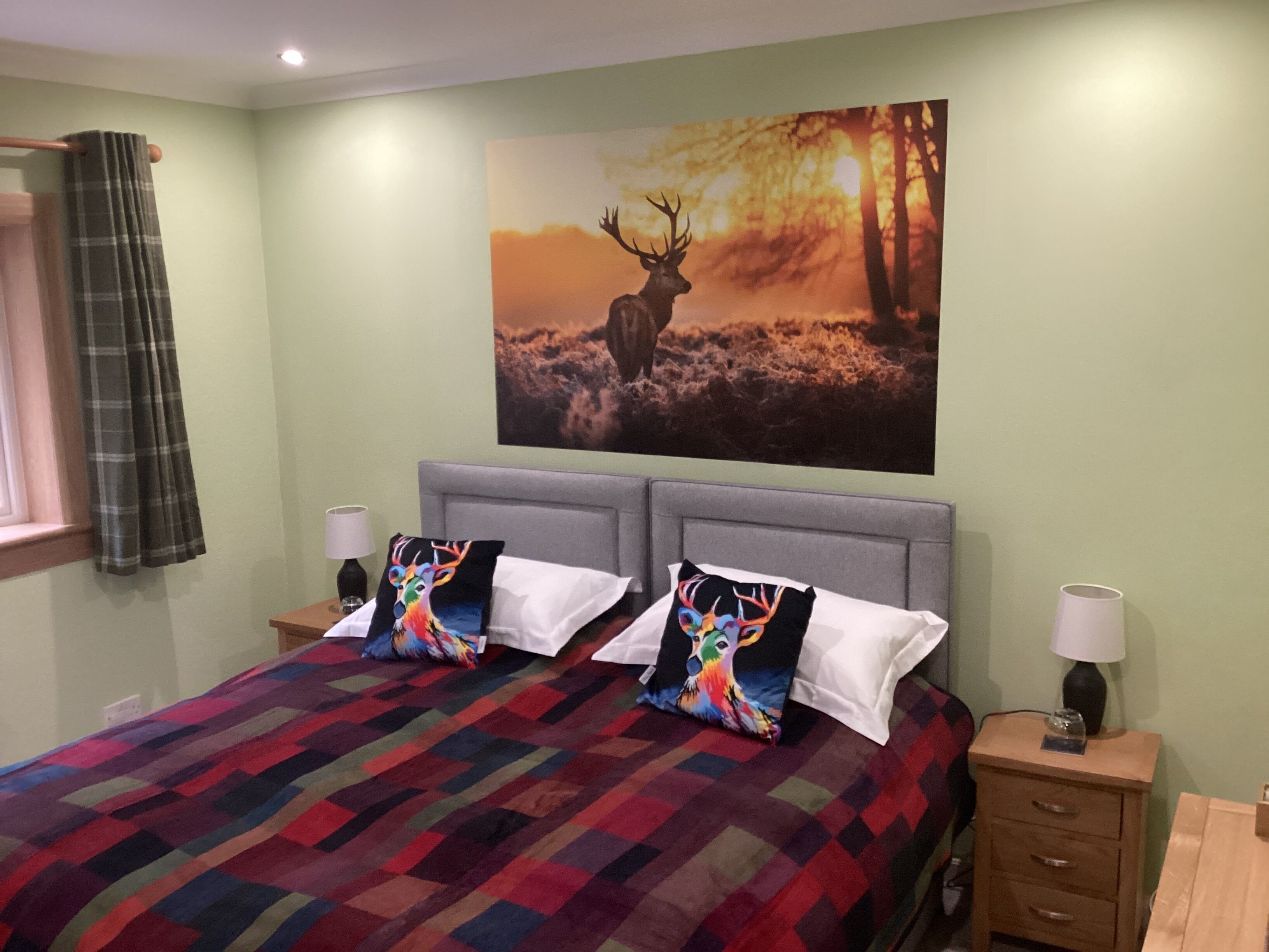 A bedroom with a large bed, two pillows, a nightstand, a lamp, and a painting of a deer on the wall.