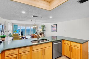 A modern kitchen with a large island, wooden cabinets, and a view of the ocean.
