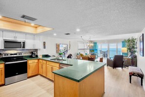 Uma cozinha moderna com ilha central, área de refeições com vista e sala de estar com varanda.