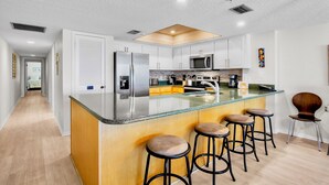 A modern kitchen with a central island, bar stools, and a microwave.