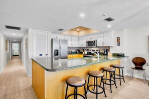 A modern kitchen with a central island, bar stools, and a microwave.