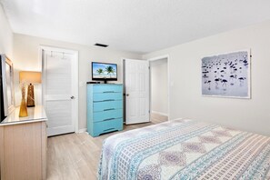 Quarto com uma cama, cômoda, televisão e um quadro na parede.