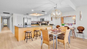 A modern kitchen with a central island, bar stools, and a dining table with wicker chairs.
