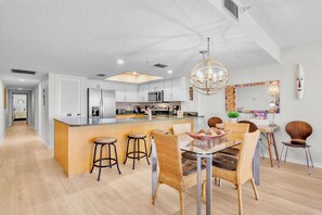 A modern kitchen with a central island, bar stools, and a dining table with wicker chairs.