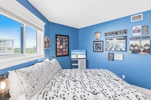 Ein Schlafzimmer mit einem großen Bett, einem Fenster und Wänden, die mit Postern und Erinnerungsstücken zum Thema Musik dekoriert sind.
