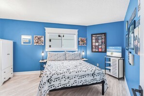 Ein Schlafzimmer mit einem Bett, einem Schrank, einem Schreibtisch und einer Wand mit gerahmten Bildern.