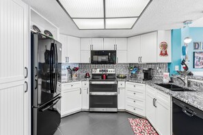 A modern kitchen with white cabinets, a stainless steel refrigerator, a microwave, an oven, and a sink.