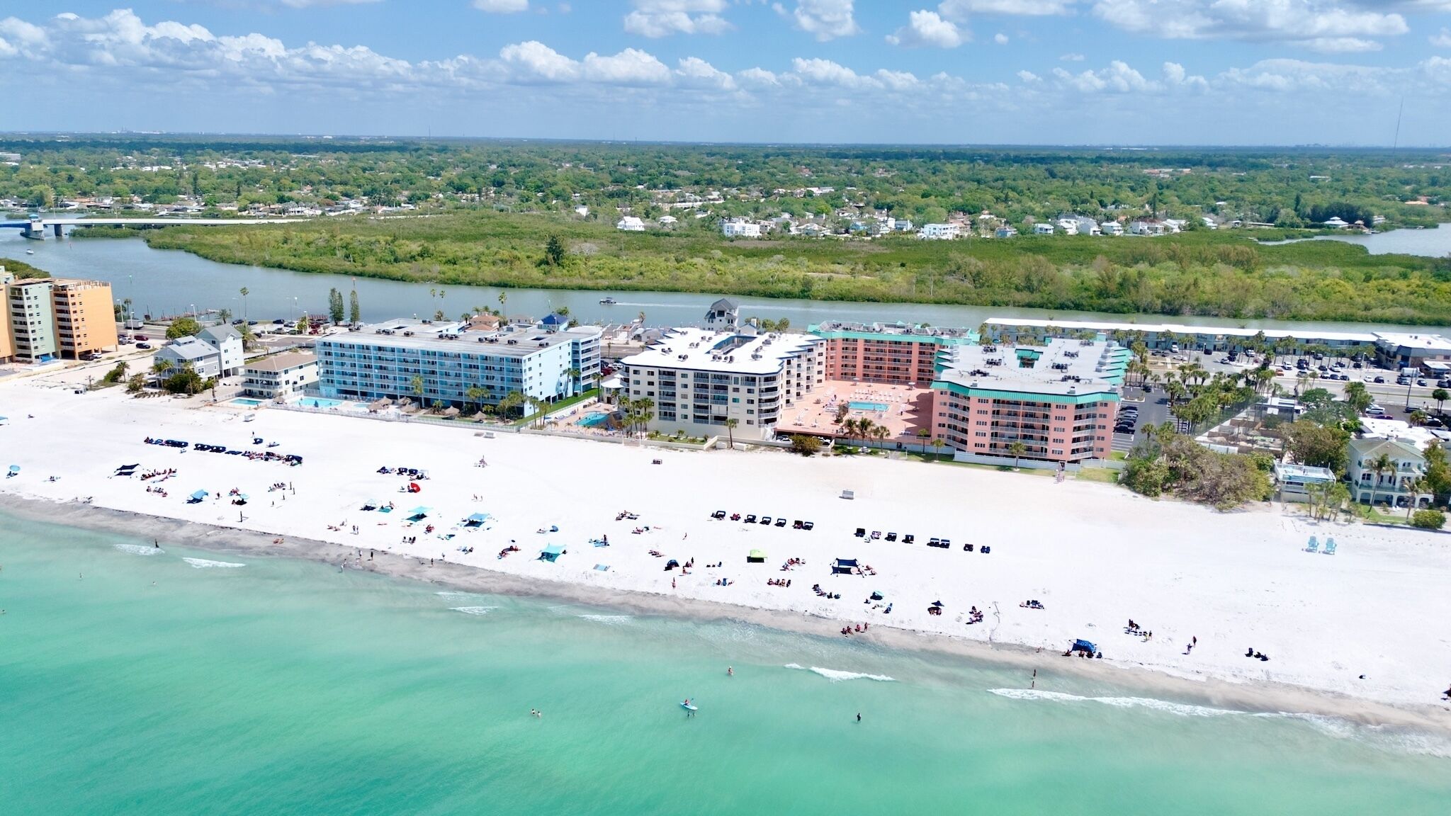 Ein Hotel an der Küste mit mehreren Gebäuden, einem Strand mit Sonnenschirmen und einem Fluss im Hintergrund.
