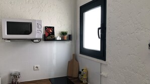 A kitchen with a white microwave, a black induction cooktop, a potted plant, and a window with a black frame.