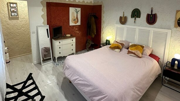 A bedroom with a bed, a dresser, a mirror, and a wall with decorative items.