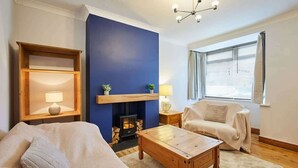 A living room with a sofa, a coffee table, a fireplace, a bookshelf, and a window with blinds. - Host & Stay | Fifth Avenue (York)