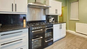 Una cocina con armarios blancos, una estufa negra y un ventanal con persianas.