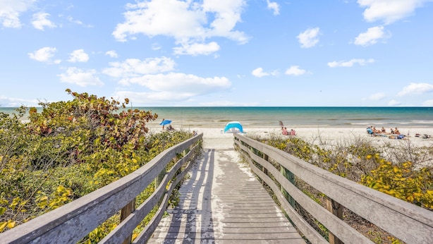 A wooden boardwalk leading to a beach with umbrellas and people relaxing. - 🏠Private Home🌴Relax on the Rocks🐬2 Blocks from Beach🌞Fire Pit and Hot Tub (Indian Rocks Beach)