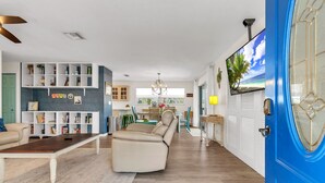 A modern living room with a beige sofa, a wooden coffee table, and a bookshelf. - 🏠Private Home🌴Relax on the Rocks🐬2 Blocks from Beach🌞Fire Pit and Hot Tub (Indian Rocks Beach)