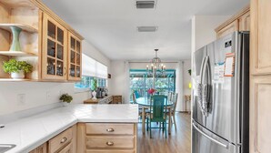 A modern kitchen with wooden cabinets, a stainless steel refrigerator, and a dining area with a chandelier. - 🏠Private Home🌴Relax on the Rocks🐬2 Blocks from Beach🌞Fire Pit and Hot Tub (Indian Rocks Beach)