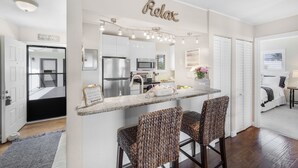 A modern kitchen with a central island, bar stools, and a 'Relax' sign above the island. - Central Condo | Pool & Short Walk to Restaurants (Marco Island)
