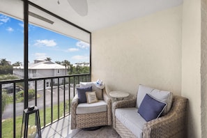 A balcony with wicker furniture, a small round table, and a view of a residential area.
