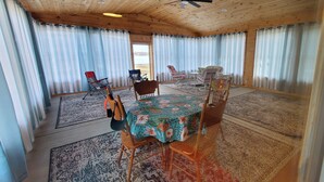 A spacious room with a wooden ceiling and large windows with curtains. There is a round table with chairs and a small table with chairs. - Hide-a-way at Swan Lake: fishing, relaxing, and dog friendly. (Allegan)