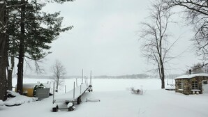 A snow-covered landscape with a dock, a small stone building, and a body of water in the background. - Hide-a-way at Swan Lake: fishing, relaxing, and dog friendly. (Allegan)