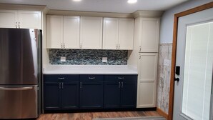 A kitchen with a stainless steel refrigerator, dark cabinets, and a tiled backsplash. - Hide-a-way at Swan Lake: fishing, relaxing, and dog friendly. (Allegan)