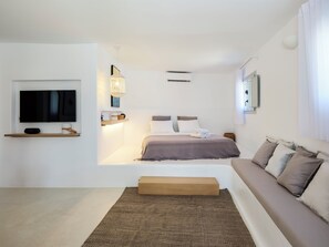 Quarto moderno com cama, sofá, televisão e ar condicionado fixado na parede.