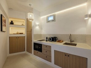 A modern kitchen with built-in appliances, wooden cabinets, and a pendant light. - MyMykonos Guest House  (greece)