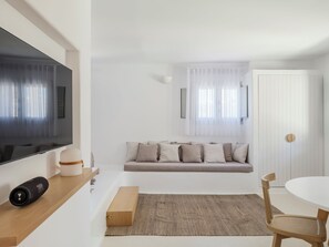 A modern living room with a flat-screen TV, a sofa with cushions, a wooden coffee table, a rug, and a dining area with a table and chairs.