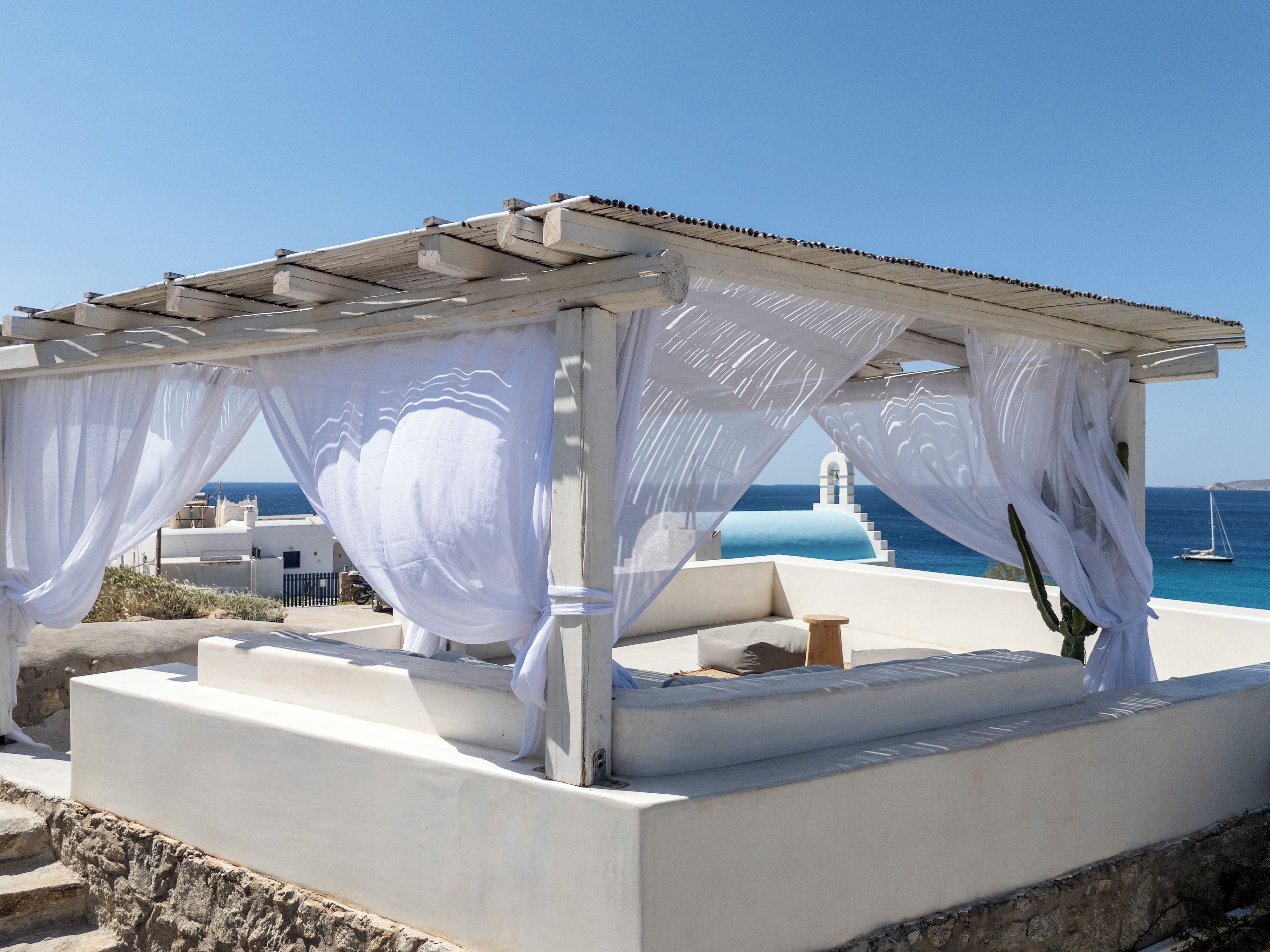 Un espace extérieur aménagé avec des sièges blancs, offrant une vue sur la mer et sur un bâtiment blanc en arrière-plan.