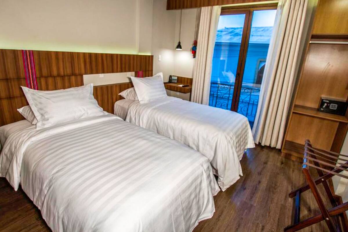 Een hotelkamer met twee bedden, een houten hoofdbord, een nachtkastje, een lamp, een stoel en uitzicht op de zee door grote ramen.