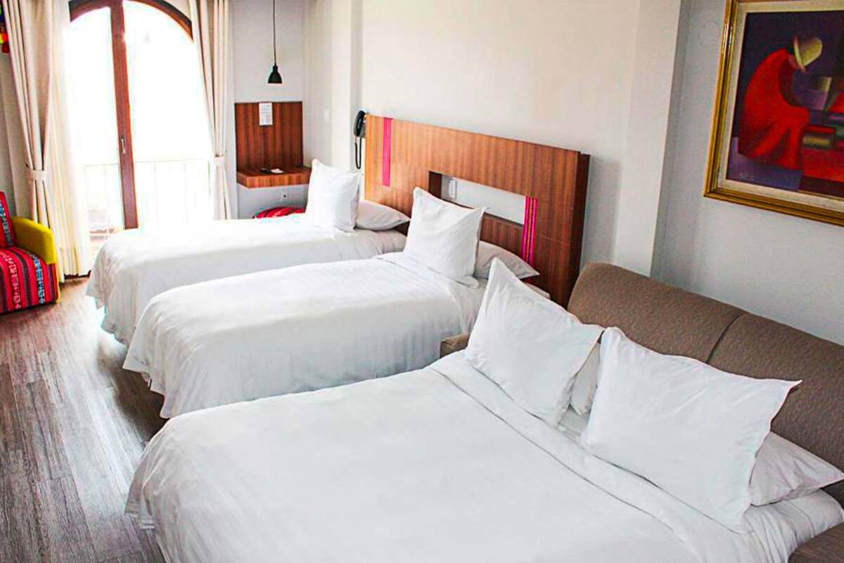 Een hotelkamer met twee bedden, een houten hoofdbord, een klein nachtkastje, een lamp en een schilderij aan de muur.