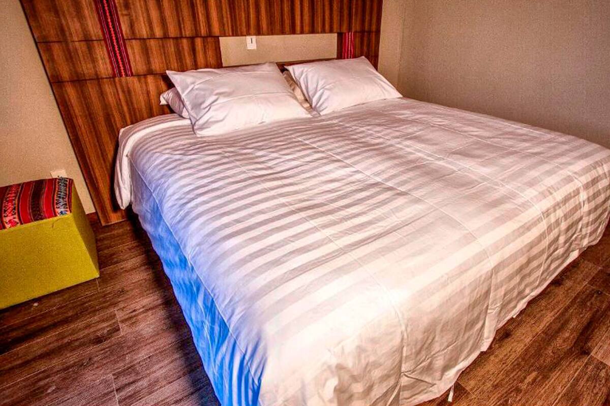 Een slaapkamer met een houten hoofdeinde, een groot bed met wit beddengoed en een houten vloer.