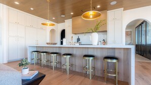 A modern kitchen with white cabinetry, a central island with stools, pendant lighting, and a view to the dining area. - Desert Sapphire at Desert Color (by Ember Stays) (St. George)