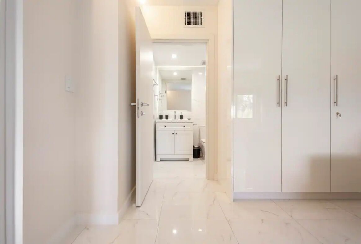 A hallway leading to a bathroom with a white sink and cabinets.