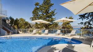A swimming pool with lounge chairs and umbrellas, surrounded by trees and a view of the sea. - Bienvenido in der Villa Los Pinos (Velilla-Taramay)