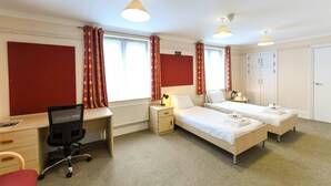 A hotel room with two single beds, a desk with a chair, a radiator, and a wardrobe. - Selwyn College (Cambridge)
