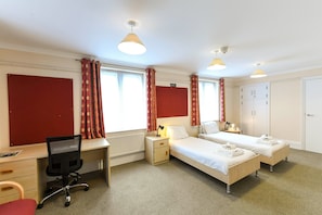A hotel room with two single beds, a desk with a chair, a radiator, and a wardrobe. - Selwyn College (Cambridge)