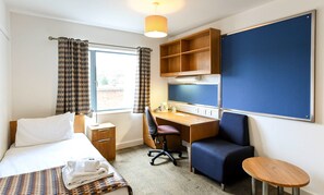 Hotellihuone, jossa on sänky, työpöytä, tuoli ja pieni pöytä.