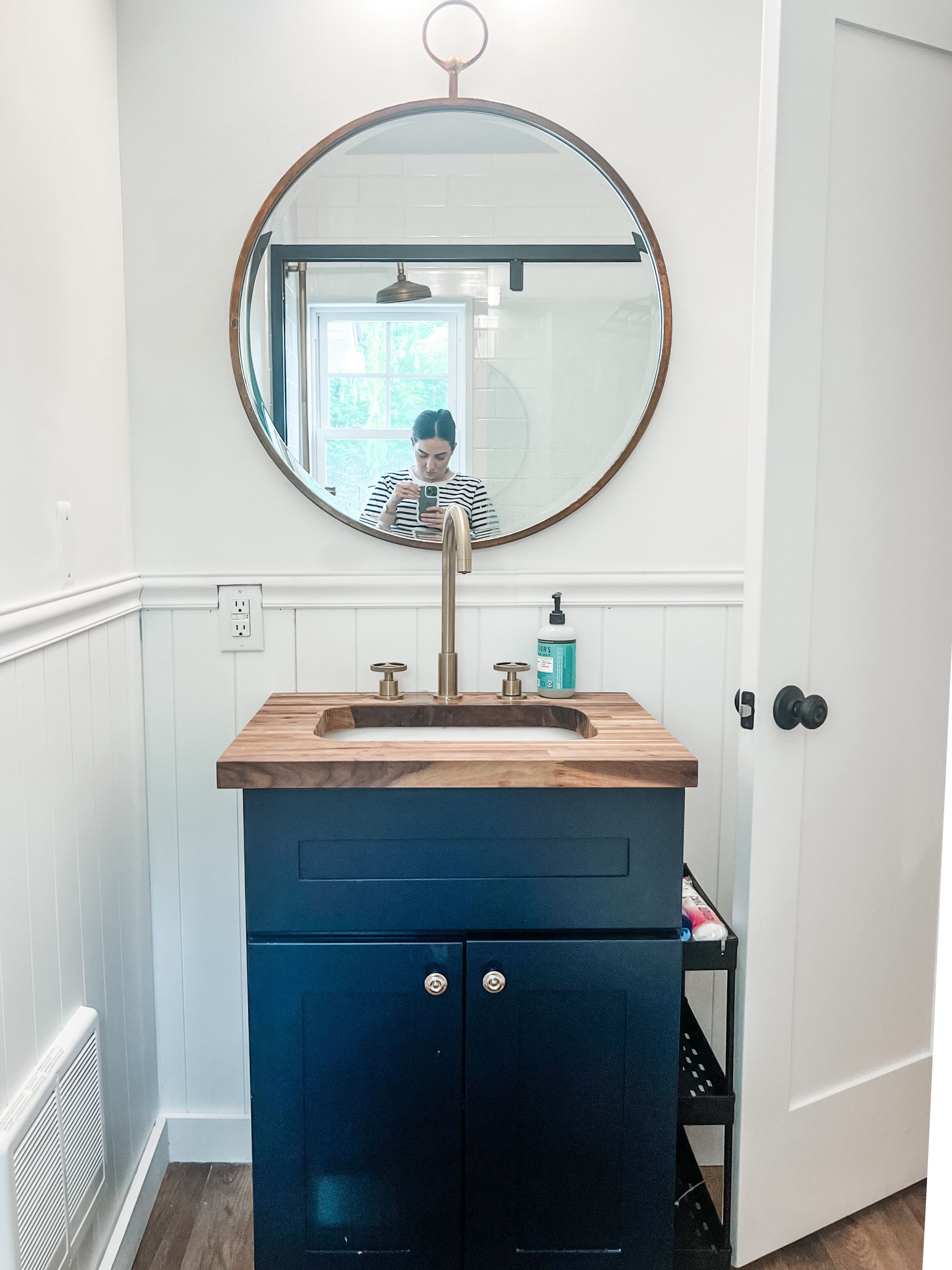 A bathroom with a wooden vanity, a round mirror, and a blue cabinet.