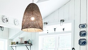 Eine Küche mit weißen Holzwänden, einer hängenden Pendelleuchte und verschiedenen Küchenutensilien auf Regalen.