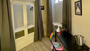 A small room with a wooden floor, a desk with a kettle, a chair, and a window with curtains. - Charming apartment with garden in Lecce (LECCE)