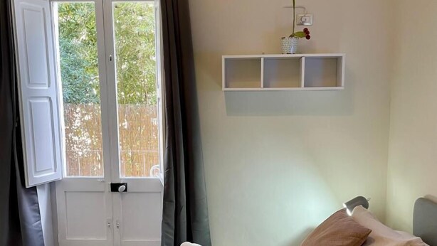 A hotel room with a bed, a window with curtains, an air conditioning unit, and a small shelf with a plant. - Charming apartment with garden in Lecce (LECCE)