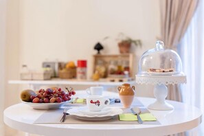 A breakfast table with a plate of fruit, a cup labeled "Quanta," a teapot, and a covered dessert stand.