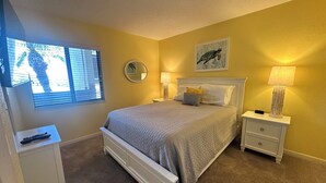 Un dormitorio con cama, mesitas de noche, lámpara, espejo y ventana con persianas.