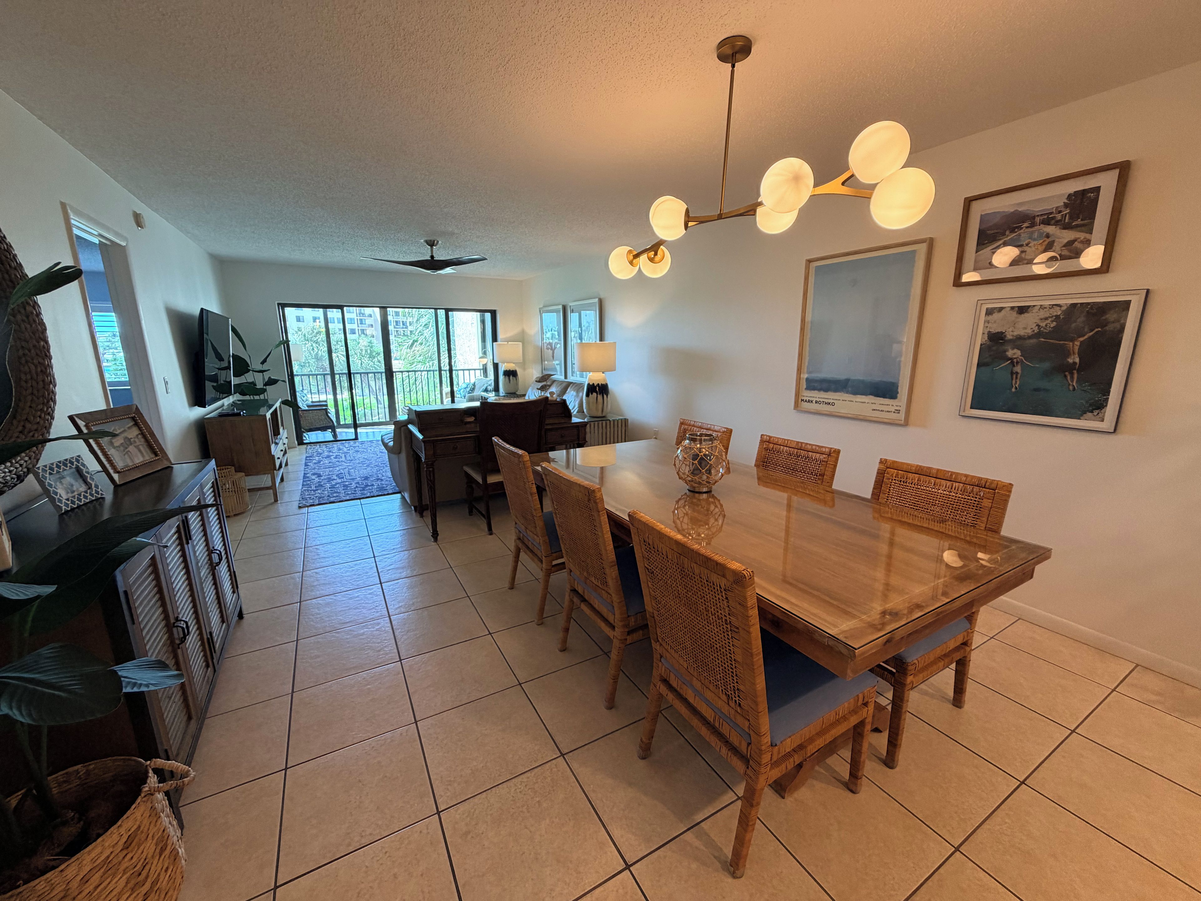A spacious dining area with a wooden table and chairs, a ceiling fan, and a large window providing natural light.