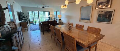 A spacious dining area with a wooden table and chairs, a ceiling fan, and a large window providing natural light.