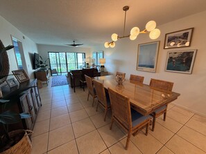 A spacious dining area with a wooden table and chairs, a ceiling fan, and a large window providing natural light.
