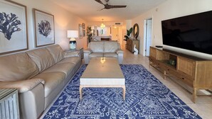 Un salon avec un canapé, une table basse et un téléviseur. Il y a un ventilateur de plafond et un tapis à motifs.