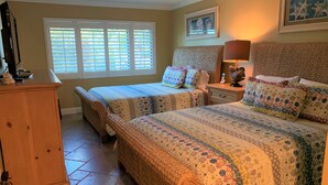 A bedroom with two beds, a dresser, a nightstand, and a window with blinds. - Contemporary Garden View, 2nd Floor (Sarasota)