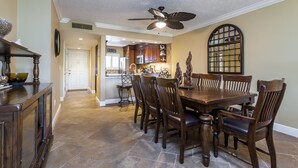 A dining area with a wooden table and chairs, a ceiling fan, and a view into the kitchen. - Contemporary Garden View, 2nd Floor (Sarasota)