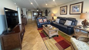 A spacious living room with a flat-screen TV, leather sofas, a coffee table, and a dining area in the background. - Contemporary Garden View, 2nd Floor (Sarasota)